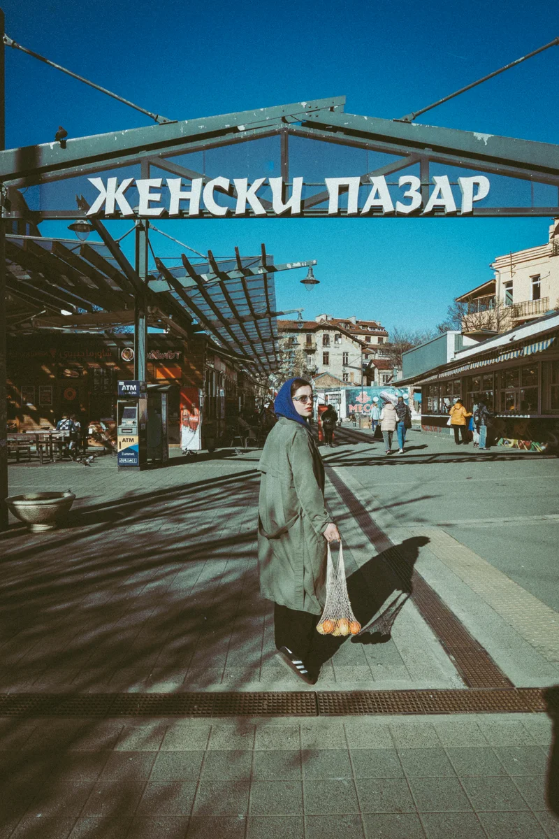 Жена с кърпа и мрежа с портокали под табелата на Женския пазар